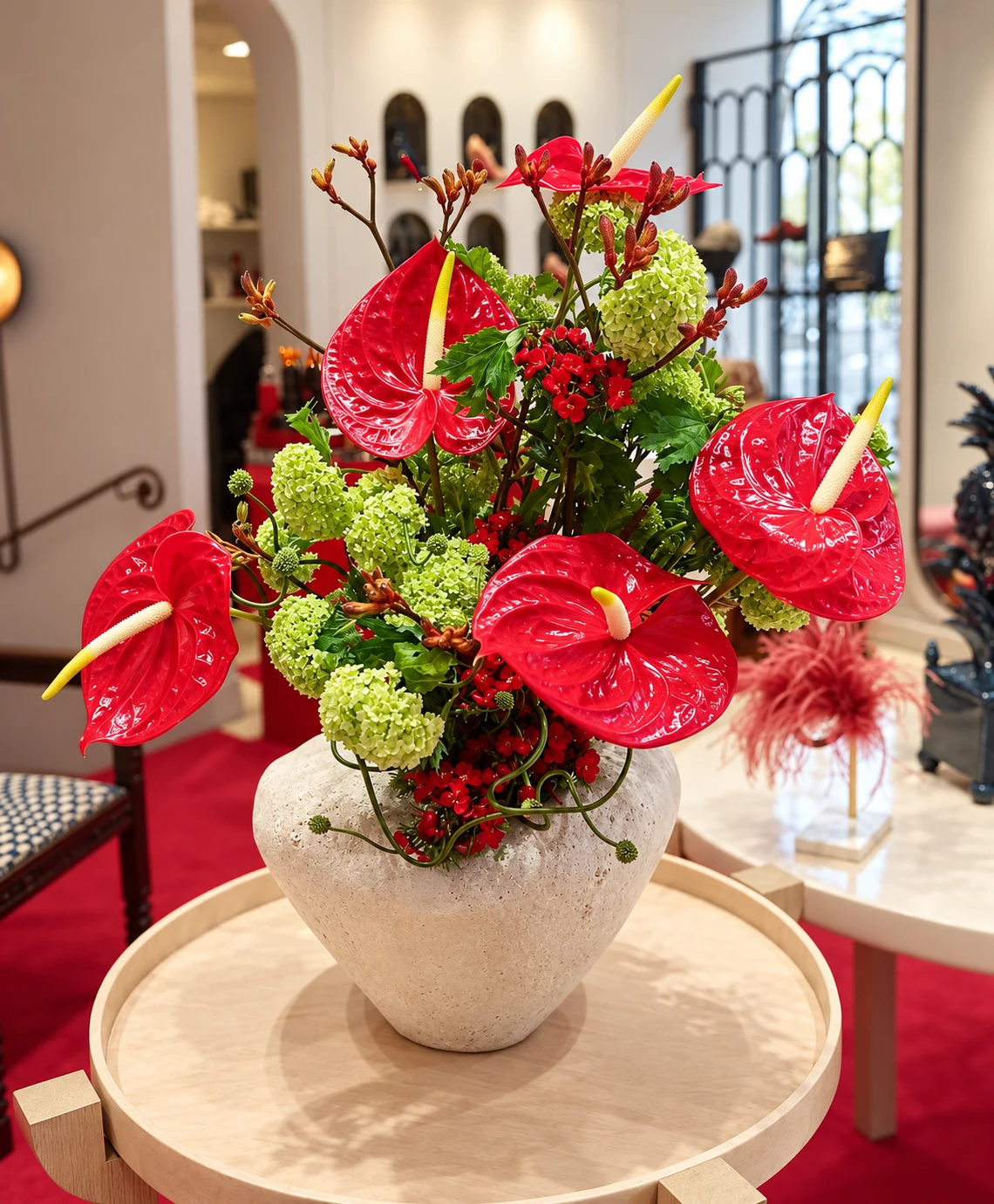 Composition florale aux anthuriums rouges et aux fleurs vert tendre dans un vase clair